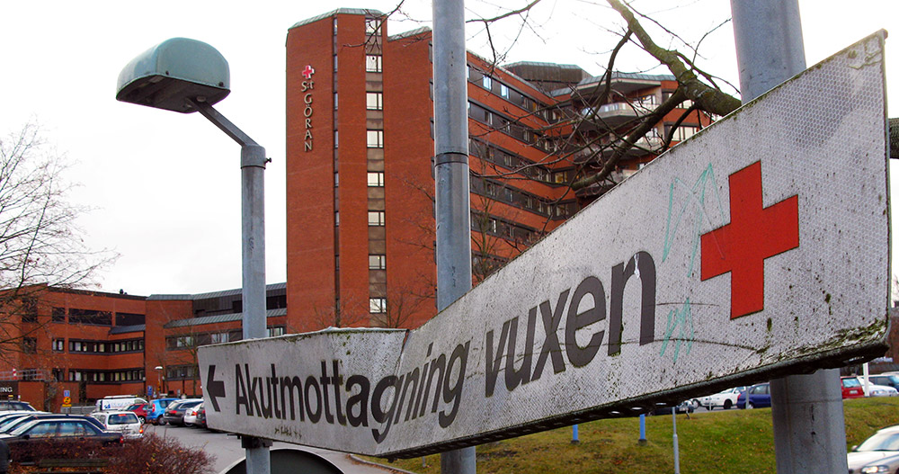En bucklig skylt med texten akutmottagning vuxen. I bakgrunden St Görans sjukhus.