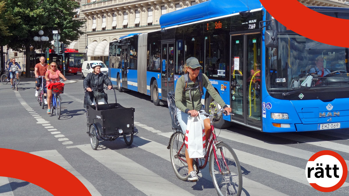 En rad cyklister kör fram i cykelfilen, intill en blåbuss, som kör åt samma håll i sin fil.