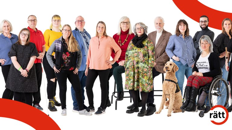 Flera olika personer står eller sitter i rullstol på rad ler mot kameran. En assistanshund sitter på golvet.