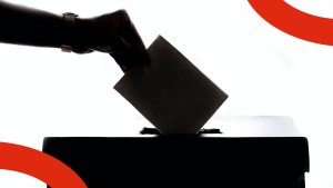 En siluett av en hand på väg att släppa ett röstkuvert ner i en röstlåda.