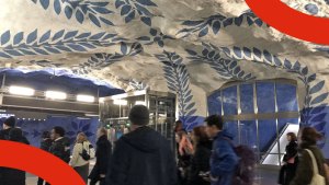 Flera personer väntar på tunnelbaneperrongen. Perrongens klippväggar och -tak är dekorerade med blå blommor.