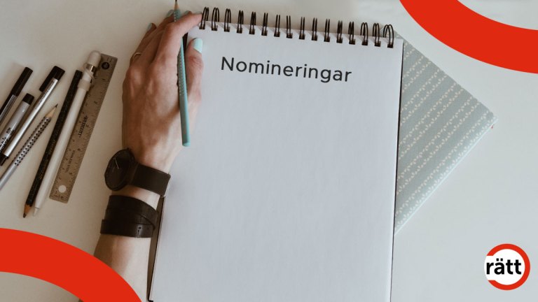 En hand som håller i en penna vilar mot en bordsskiva. På bordet ligger flera pennor och ett skrivblock med texten nominera.