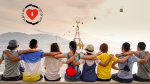 En lång rad med människor sitter tillsammans med armarna om varandras ryggar och spanar ut mot det stora vattendraget framför dem och kullar och berg som avtecknar sig mot horisonten.