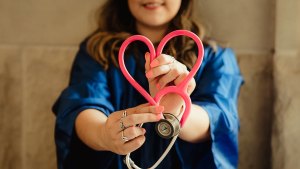 En leende person håller fram ett rosa stetoskop, som har formats till ett hjärta.