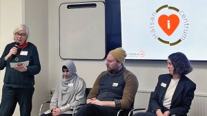 Annika Hässler står och läser upp en fråga i mikrofon. Panelen sitter främst i lokalen och lyssnar.