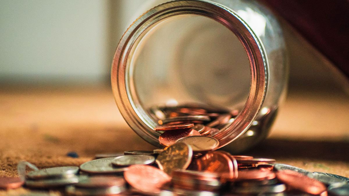 En mängd mynt väller ut ur en glasburk, som lagts på sidan.