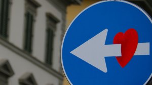 En trafikskylt där en vit pil går igenom ett påklistrat rött hjärta.