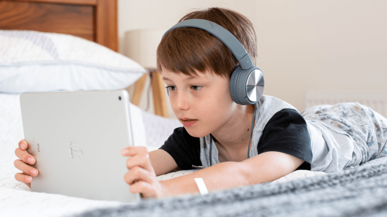 Ett barn med hörlurar på öronen ligger ner och tittar på något på en surfplatta.