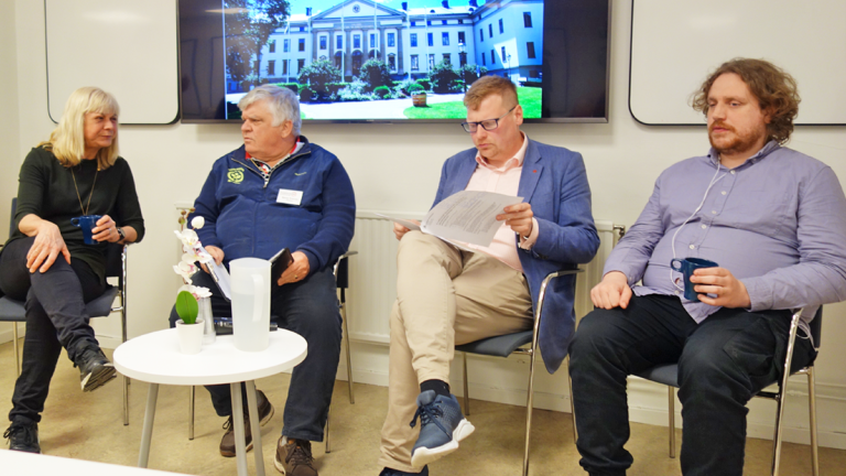 Paneldeltagarna i mötet om rätten till arbete sitter på rad. På skärmen bakom dem står det att det för närvarande är fika rast. Några paneldeltagare pratar med varandra. En kikar i sina papper.