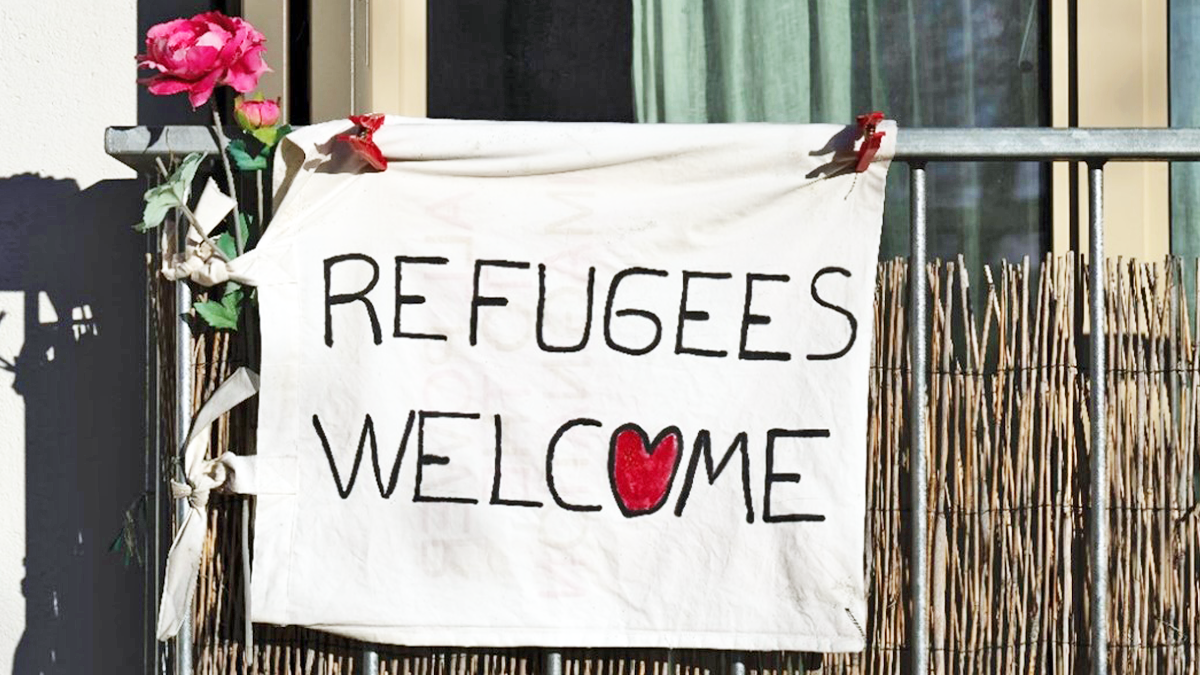 Ett vitt skynke där det står Refugees Welcome, flyktingar välkomna. O:et är i formen av ett rött hjärta. Skynket sitter på en balkong.