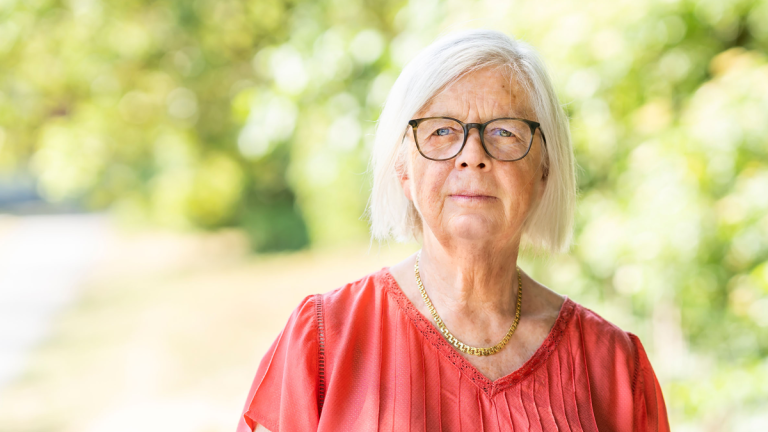 Annika Hässler ser bestämd ut. Hon har på sig en röd tröja och glasögon. I bakgrunden syns träd och växtlighet.