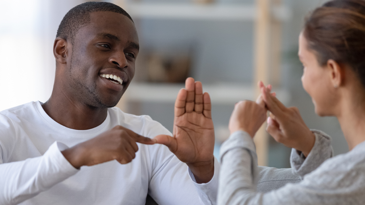 En man och en kvinna kommunicerar med teckenspråk. De har olika hudfärg.