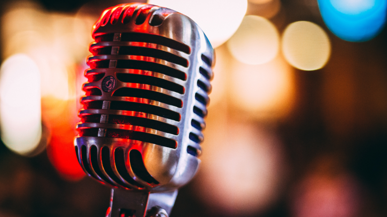 En gammeldags mikrofon. Färgglada lampor syns i bakgrunden och speglas i mikrofonen.