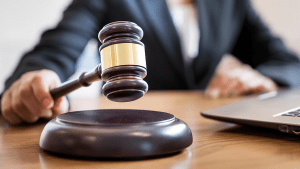 En person med en ordförandeklubba i handen och en öppen bärbar dator framför sig på bordet.