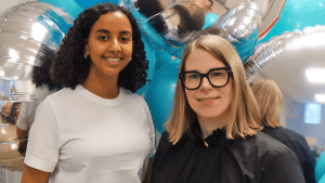 Handläggarna Salina och Karin framför en vägg av blå och silverfärgade ballonger.