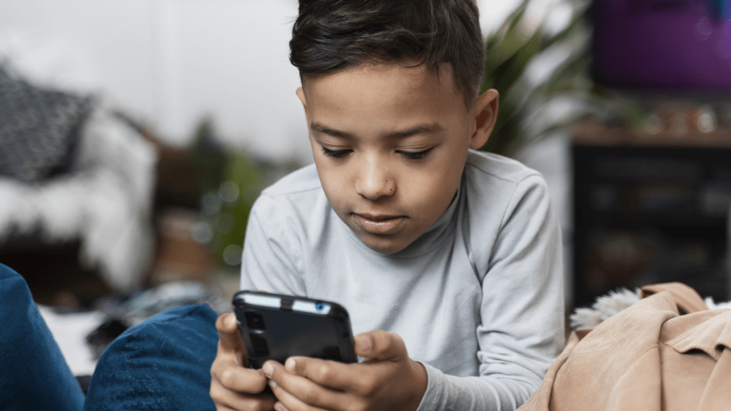 Pojke i vardagsrum lutar sig mot soffryggen och spelar på sin mobiltelefon