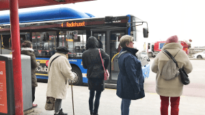 Flera personer står i rad och väntar på att bussen som just rullat in ska öppna dörrarna.