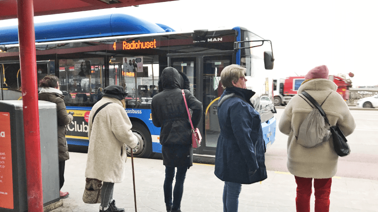Flera personer står i rad och väntar på att bussen som just rullat in ska öppna dörrarna.