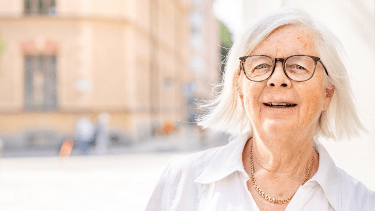 Annika Hässler i vit skjorta ler in i kameran. I bakgrunden ett sommarsoligt Kungsholmen.