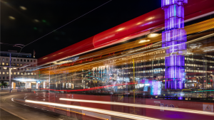Nattrafiken på Sergels torg. Neonljus och upplysta reklamskyltar skymtar. Kamerans slutare har varit öppen länge och fångat röda och vita streck. Det är en suddig, men identifierbar, passerande röd sl-buss. I bakgrunden lyser glaspelaren Kristallvertikalaccent svalt lila.