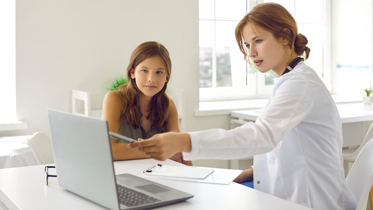 En läkare pekar ut något på en datorskärm för en tonåring. Båda ser mot skärmen.