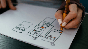 En handritad modell av en app under utveckling. En hand fyller i detaljer med en orange penna.