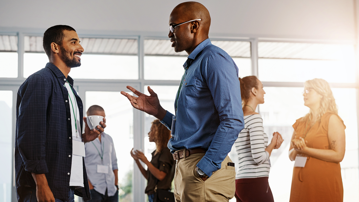 Sex personer diskuterar två och två, uppdelade i tre små grupper. De flesta har ett grönt band med en plastbricka runt halsen. En person håller i en kaffemugg.