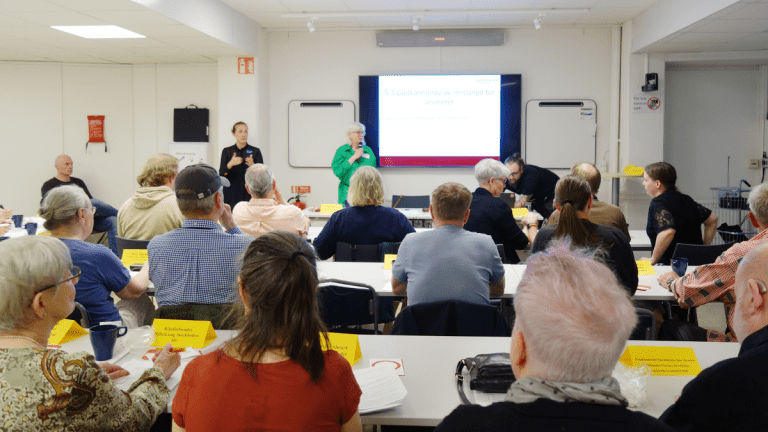 Stora rummet i ÅttiotvåAn är fullt av personer som lyssnar på Annika Hässler, som talar i en mikrofon, längst fram i salen.