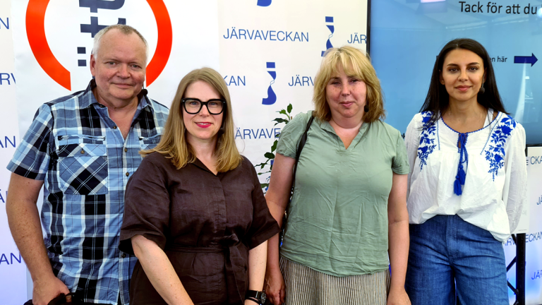 Fyra personer står på rad och tittar glatt in i kameran. I bakgrunden skymtar en flagga med Funktionsrätt Stockholms län och en back drop med Järvaveckan.