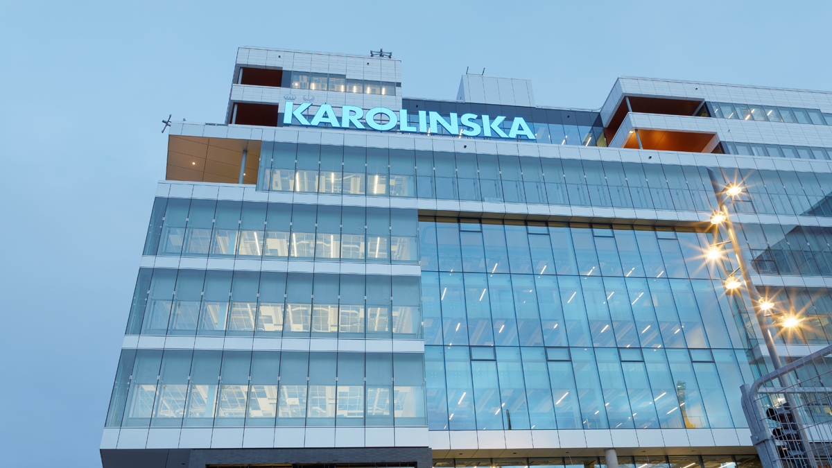 En byggnad med väldigt mycket glasfasad. Högt uppe på byggnaden sitter en ljusskylt som upplyser om att det är Karolinska sjukhuset.