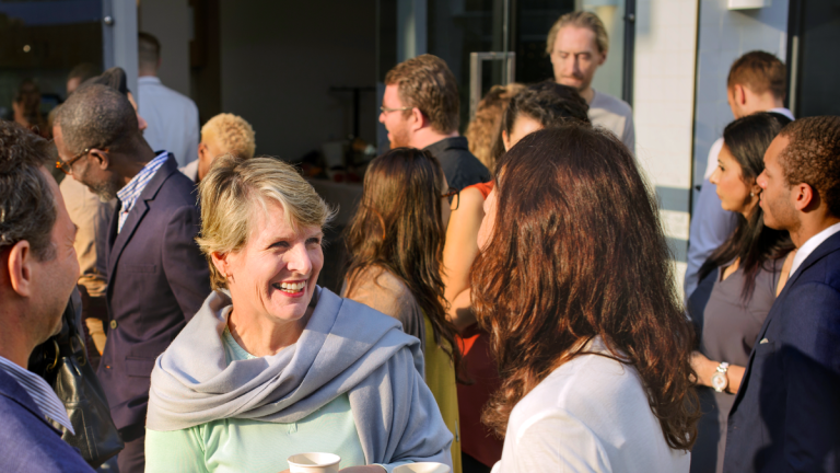 En stor grupp människor står i mindre grupper och samtalar. De ser glada ut.