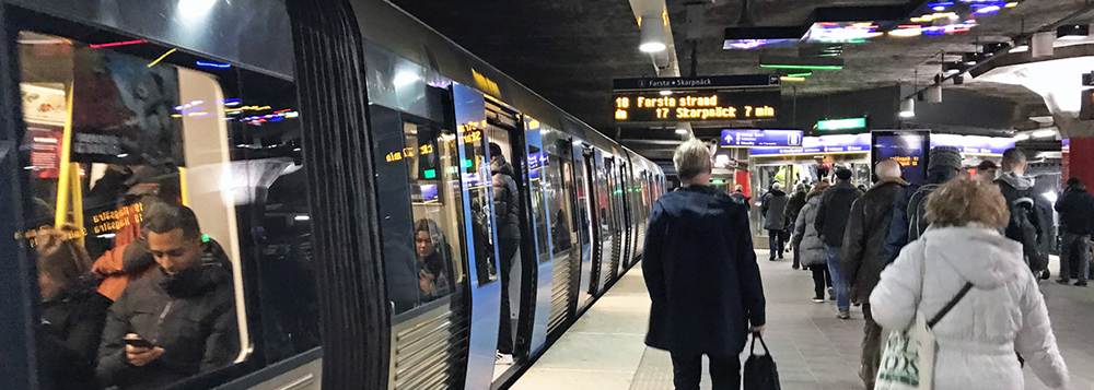 Ett tunnelbanetåg vid en perrong. Många människor rör sig på perrongen.