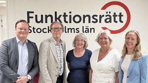 Fem personer står på rad framför en vägg med vår logga på. De ler in i kameran.