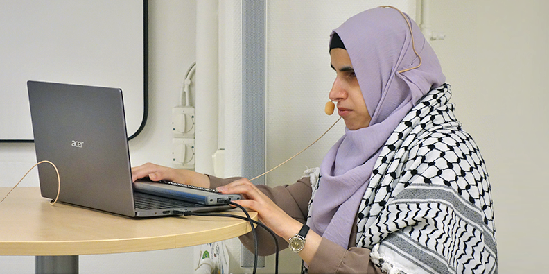 Doaa Zatara står vid ett ståbord och håller händerna på sin laptop. 
