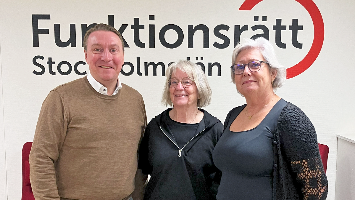 Tre personer står på rad framför en vägg med vår logga på. De ler in i kameran.