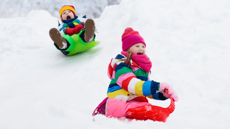 Två barn åker stjärtlapp i snön.