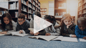 En play-knapp ligger ovanpå en bild av inbjudan till vår tema-lansering inför 2025. Bilden är av en vuxen kvinna omgiven av fem barn i ett bibliotek. Alla har något läsbart framför sig och ser ut att läsa.