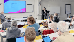 Johanna står längst fram i den fullsatta salen och berättar om sin presentation, som syns på en skärm i bakgrunden.