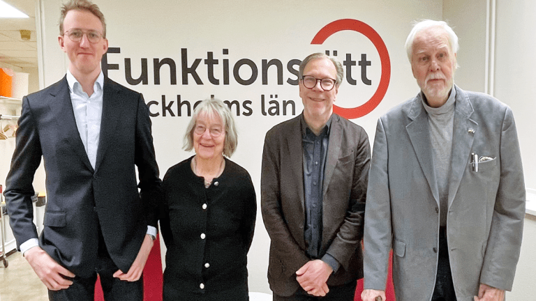 Fyra personer står på rad framför Funktionsrätt Stockholms läns logga. Alla ler mot kameran.