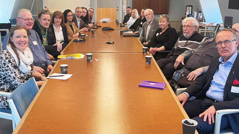 Flera personer kring ett långt träbord. De flesta ler mot kameran.