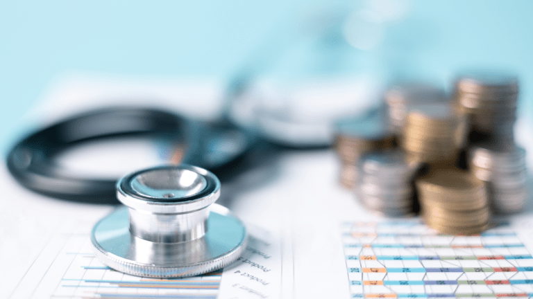 På papper med olika diagram ligger ett stetoskop och flera små pelare av mynt, staplade på varandra.