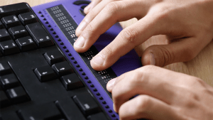 Ett par händer vilar på ett tangentbord som kontrolleras med punktskriftstangenter.
