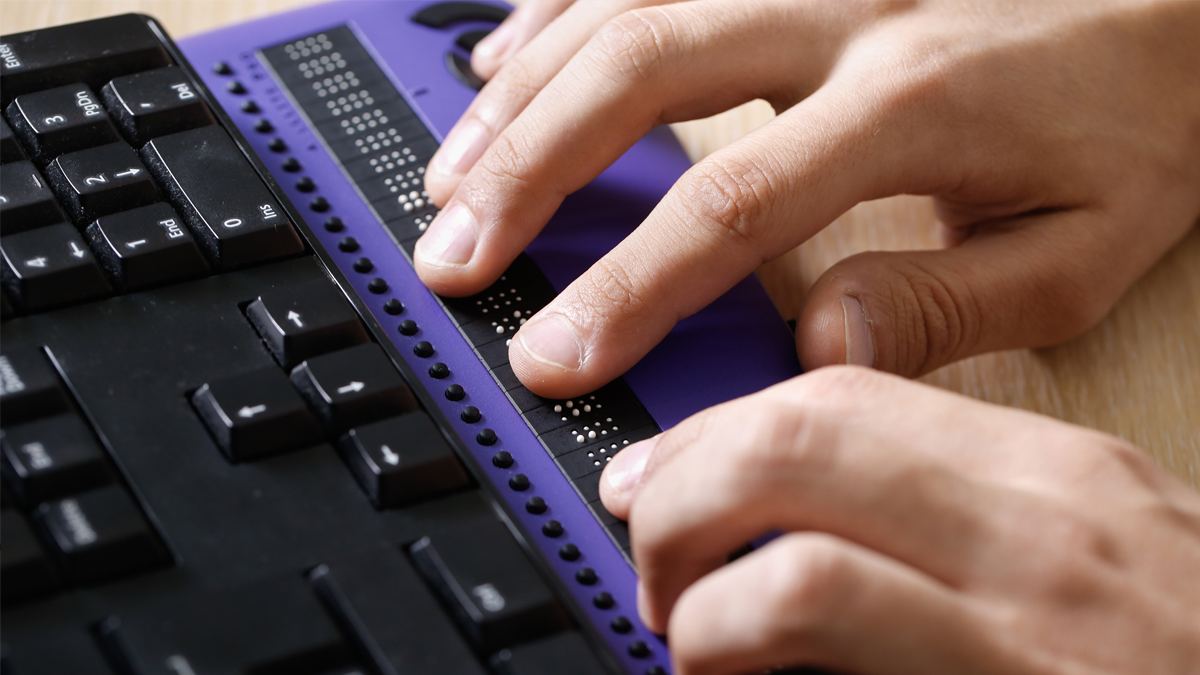 Ett par händer vilar på ett tangentbord som kontrolleras med punktskriftstangenter.