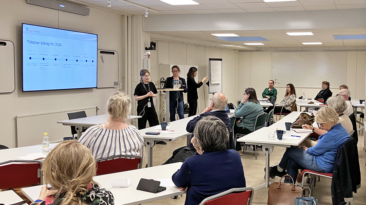 Flera personer i konferenslokalen ÅttiotvåAn sitter med uppmärksamheten riktad mot två talare längst fram i lokalen och deras presentation om bidrag 2026, som skymtar på en skärm bakom dem.