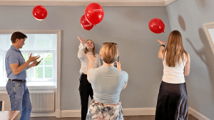 insiktsutbildning för Centerpartiet. Fyra personer kämpar för att hålla några röda ballonger i luften, samtidigt som de skickar ett meddelande på sina mobiltelefoner.