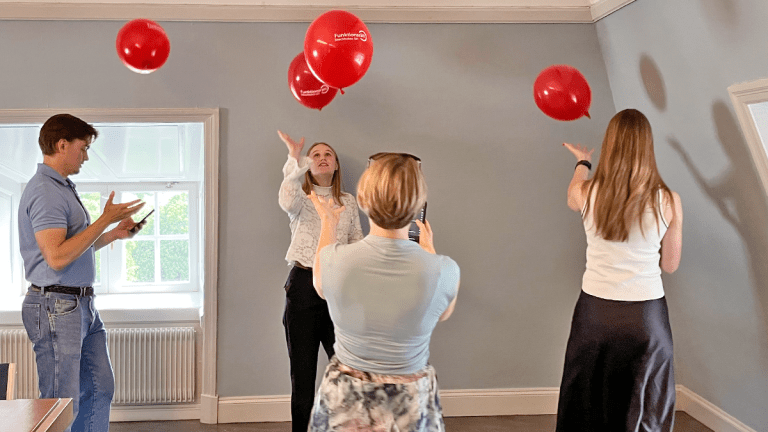insiktsutbildning för Centerpartiet. Fyra personer kämpar för att hålla några röda ballonger i luften, samtidigt som de skickar ett meddelande på sina mobiltelefoner.
