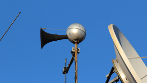 En ljudsändare i systemet för utomhusvarning, Viktigt Meddelande. Ljudsändaren ser ut som en silverfärgad boll med en svart strut på ena sidan.
