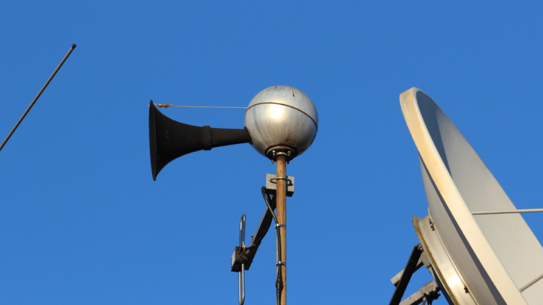 En ljudsändare i systemet för utomhusvarning, Viktigt Meddelande. Ljudsändaren ser ut som en silverfärgad boll med en svart strut på ena sidan.