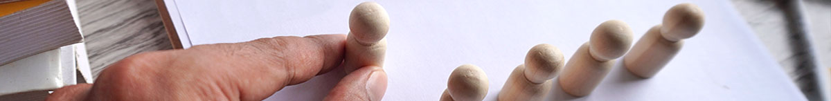 En rad små träfigurer står på pappret. En hand håller i ännu en träfigur och ställer den på pappret med de andra figurerna. Nominera till val 2026.