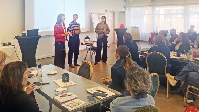 Vår handläggare Ida står längst fram i en sal och talar. Salen är fylld med deltagare.